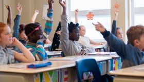 Multi-ethnic students sit into the class with arms raised