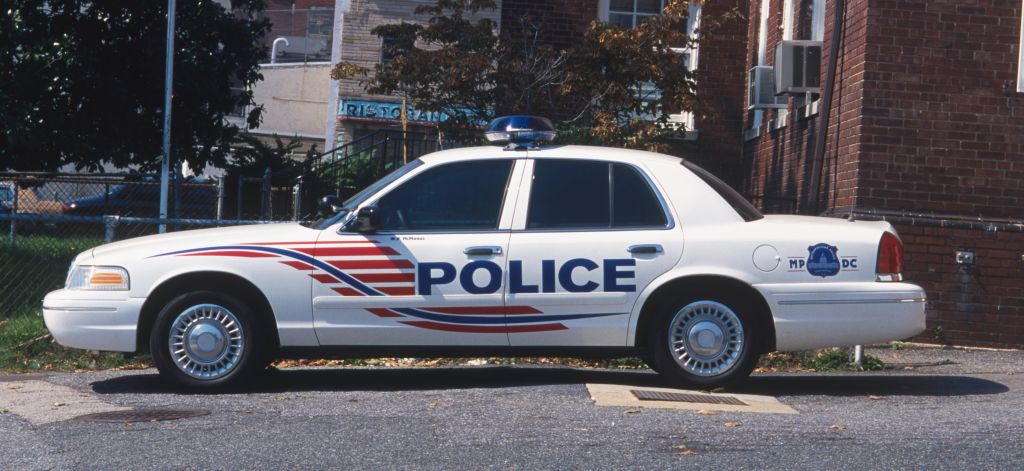USA, Washington DC, police car parked outside police station next to stars-and-stripes flag on a mast, side view