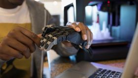 Close up male designer examining robotic hand prototype at laptop next to 3D printer