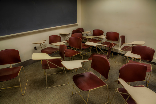 Empty chairs and desks randomly placed in a college classroom.