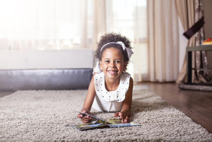 Beautiful little girl reading a book on the carpet.