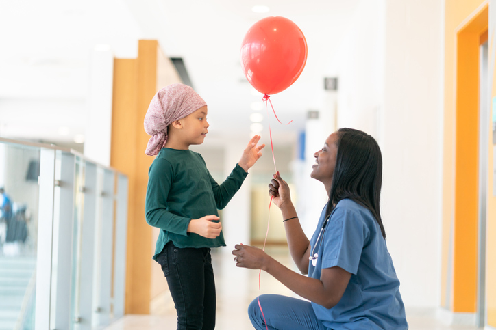 Doctor gives a red balloon to a little girl with cancer
