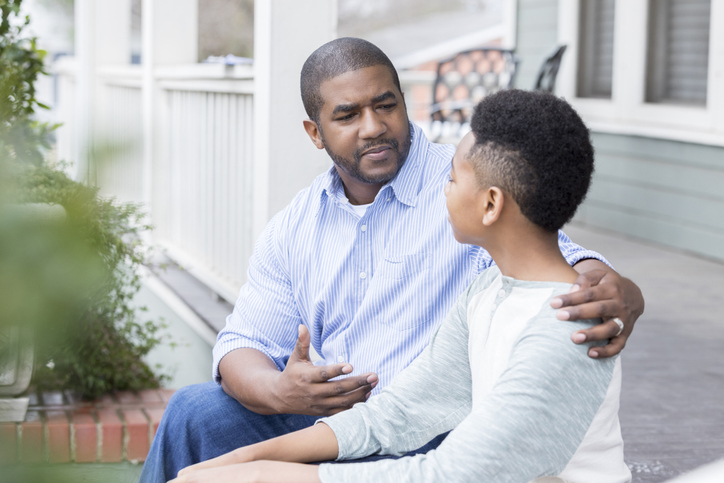 Concerned father sits on porch with preteen son