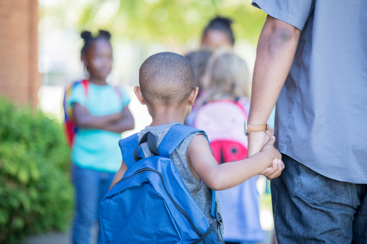 African American preschool age little boy holds his father's hand while walking to first day of kindergarten