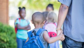 African American preschool age little boy holds his father's hand while walking to first day of kindergarten