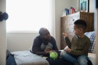 Father and son depositing coins into piggy bank in bedroom