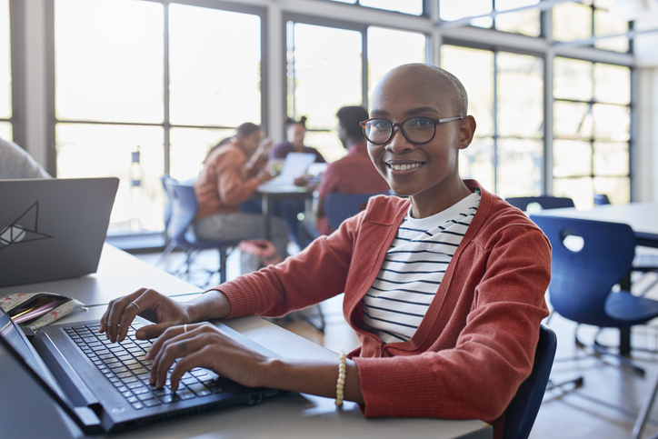 Smiling bald young woman using laptop in classroom