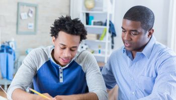 Confident father helps teenage son with homework