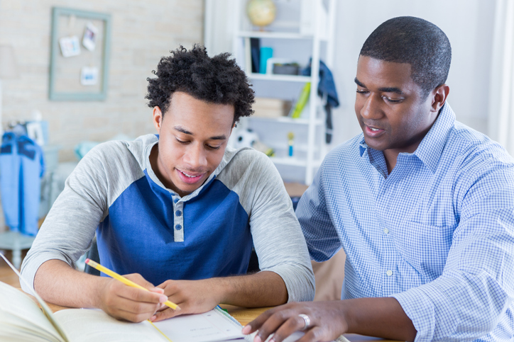 Confident father helps teenage son with homework