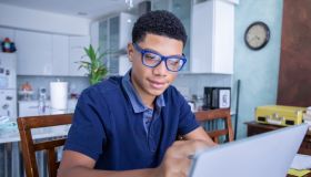 Smart teenage boy uses laptop computer to do homework in kitchen