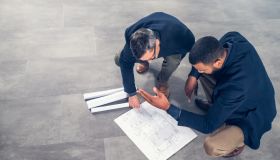 Architects talking about blueprints while crouching on the floor