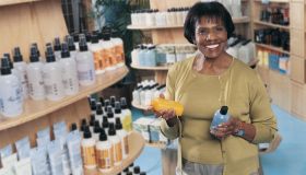 Smiling Woman in a Pharmacy Holding Bottles of Shampoo