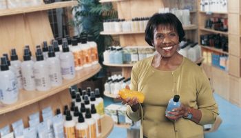 Smiling Woman in a Pharmacy Holding Bottles of Shampoo