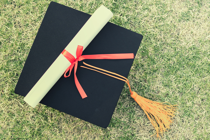 Close-Up Of Mortarboard And Diploma On Grassy Field
