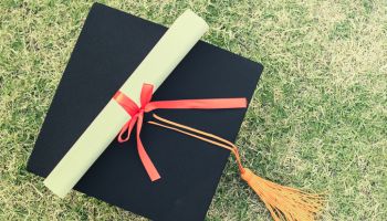 Close-Up Of Mortarboard And Diploma On Grassy Field