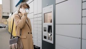 Woman on the phone wearing face mask and gloves near a parcel terminal
