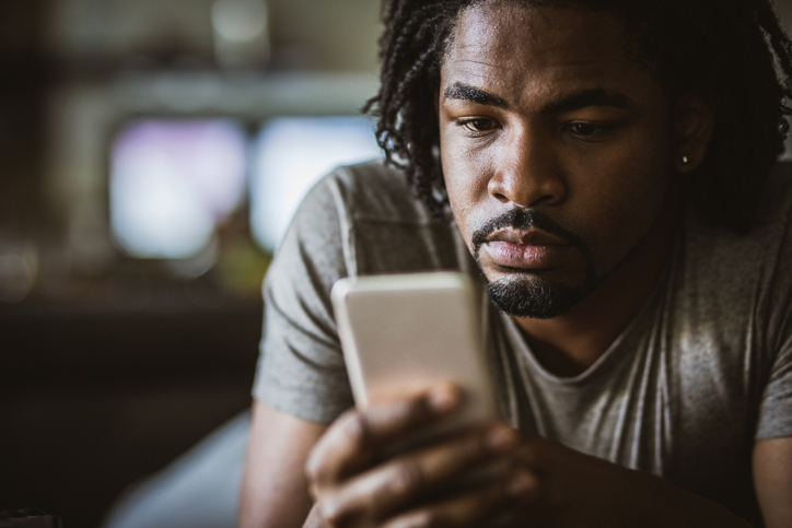 Young black man text messaging on smart phone at home.