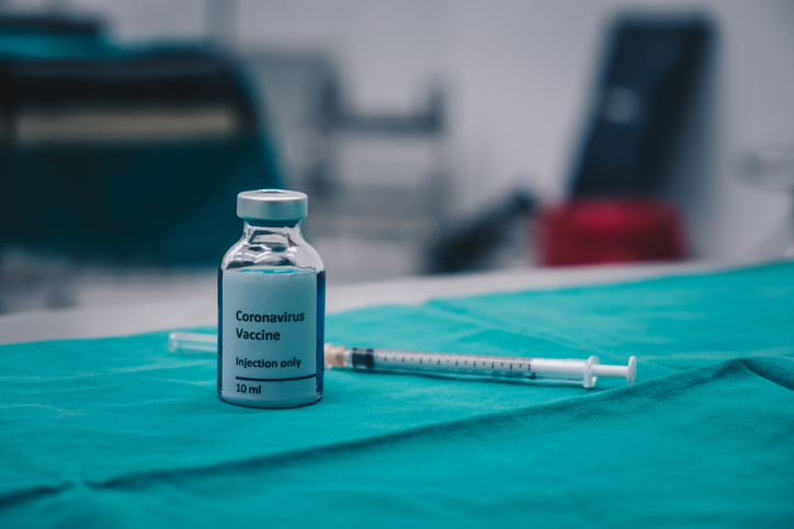 A sample test bottle of Covid-19 vaccine with needle syringe on table in hospital.