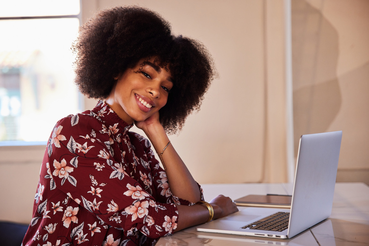 Smiling young woman sitting alone at a table and working on her laptop