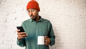 Man with coffee cup using smart phone against white brick wall