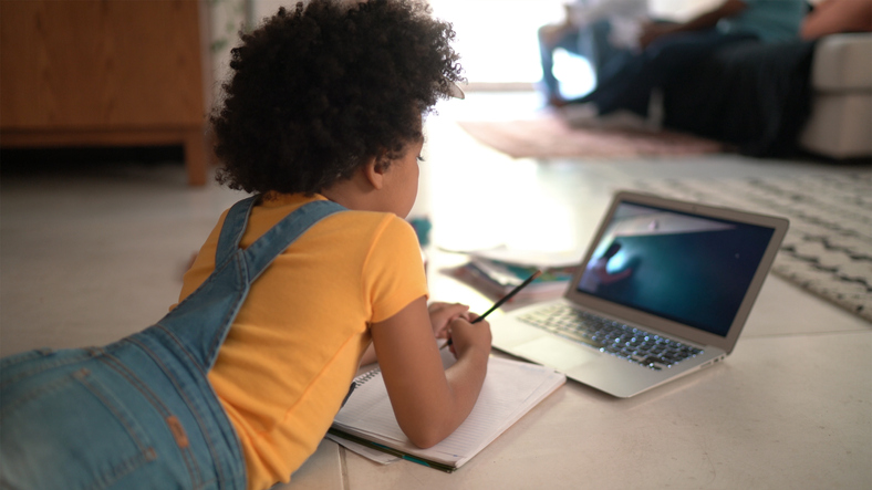 Rear view of a elementary age girl studying watching online classes at home