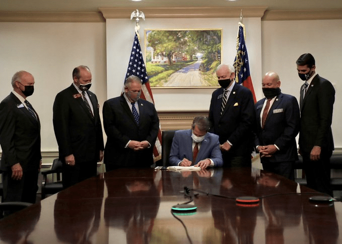 Georgia Gov. Brian Kemp signs voter suppression laws in front of painting of slavery plantation