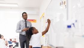 Primary school girl standing next to the white board, answering the question in the classroom.