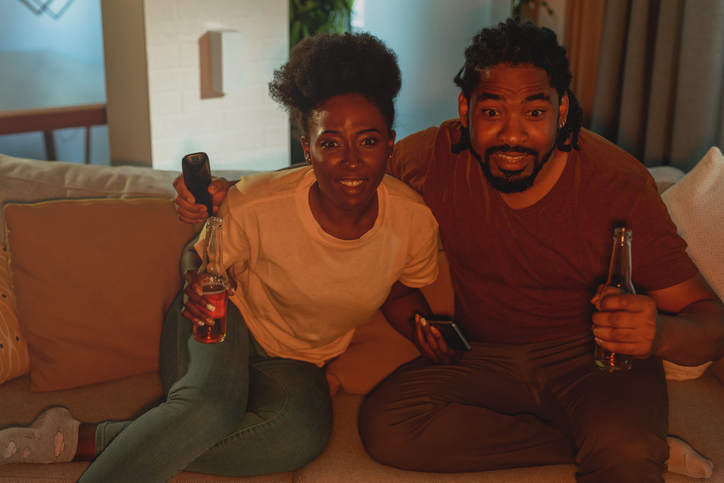 Couple relaxing on the couch at home, watching sports and cheer for their team