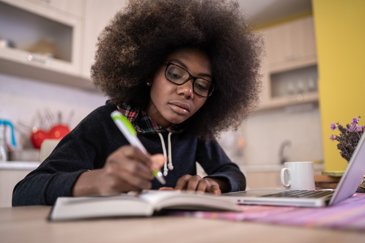 Young african american girl with glasses working and studying at home on a laptop. Covid-19 isolation, home activities