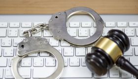 Laptop, wooden gavel and handcuffs on light table, closeup. Cyber crime