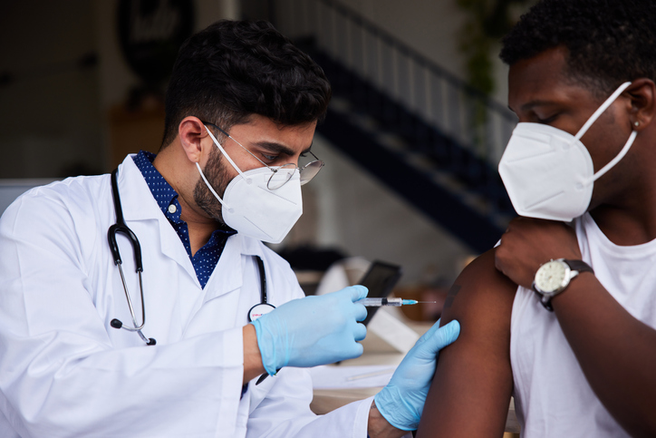 Doctor wearing a mask giving a male patient a vaccination in a clinic