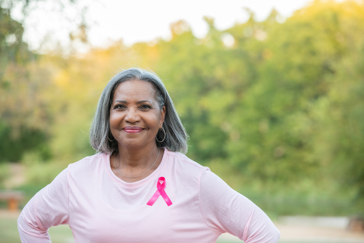 Senior woman with pink breast cancer ribbon on her shirt smiles while looking at the camera