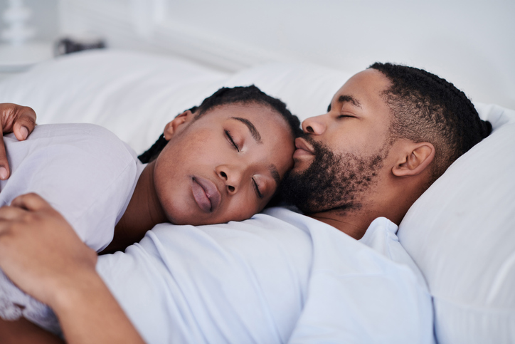 Shot of a young couple cuddling while sleeping in bed together at home
