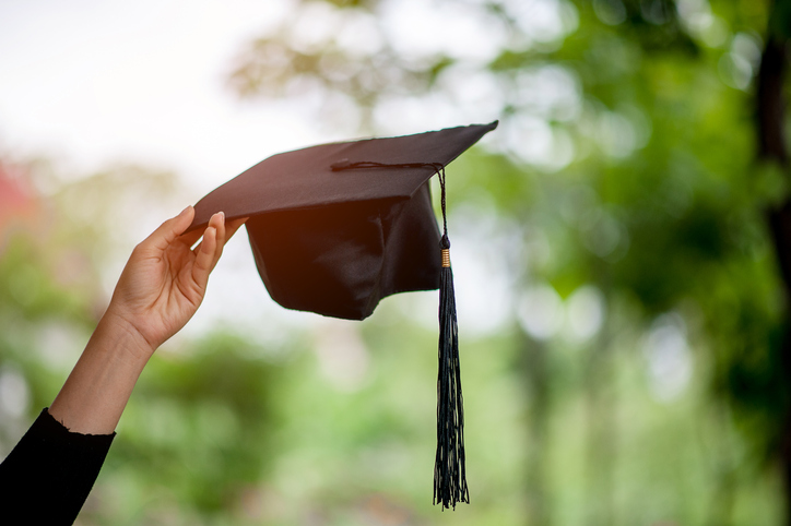 Close-Up Of Cropped Hand Holding Mortarboard Against Blurred Background