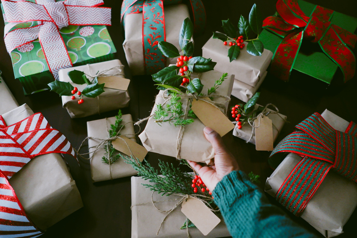 Woman Holds Christmas Present Adorned With Juniper and Holly Branches