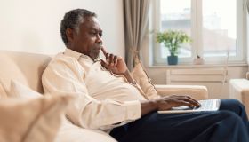 Senior Man Sitting On Sofa Using Laptop At Home