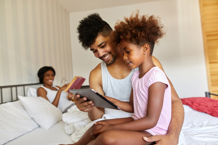 Father and daughter sitting on bed using digital tablet