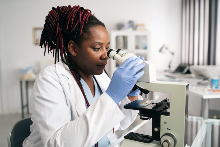 African-american scientist woman or graduate student in a lab coat and protective face mask works in modern laboratory