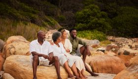 Smiling young couple sitting with their senior parents on rocks at the beach