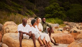 Smiling young couple sitting with their senior parents on rocks at the beach