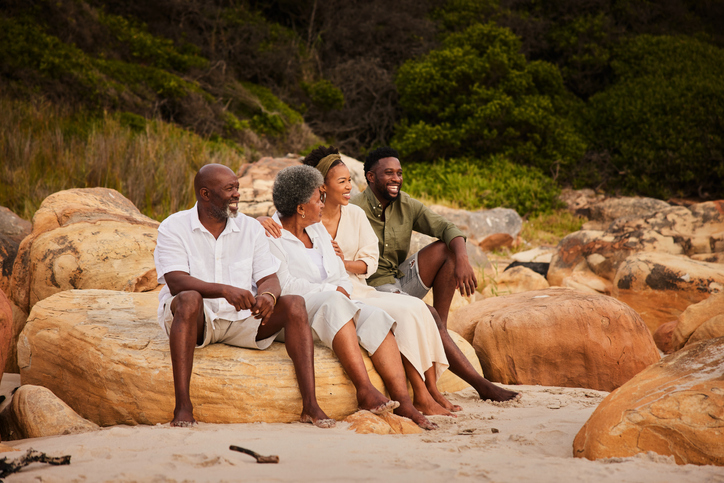 Smiling young couple sitting with their senior parents on rocks at the beach