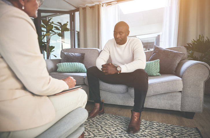 A man talking to a psychologist or therapist. A young african american guy looking sad while getting help during a therapy session with a counsellor