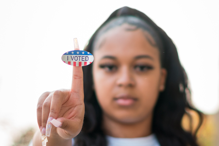Young woman holds up "I voted" sticker