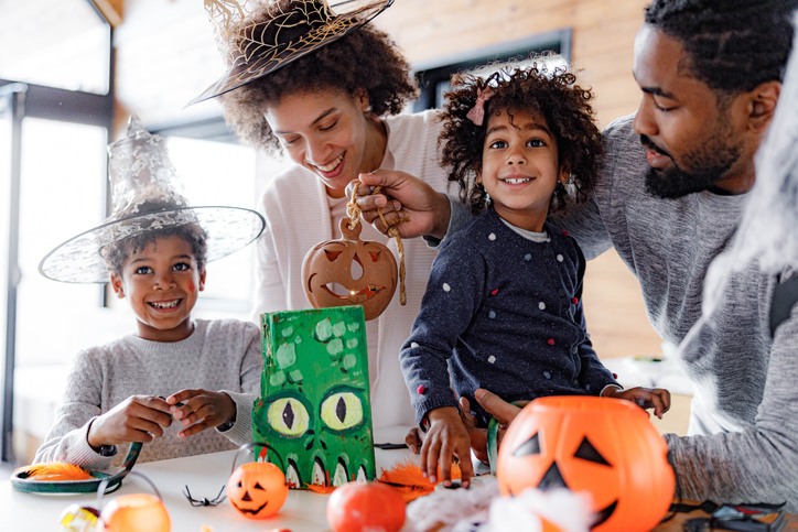 Happy black parents and their kids making decorations for Halloween at home.