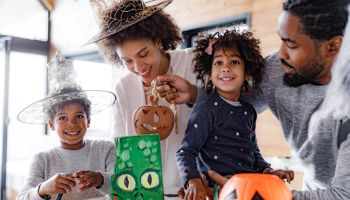 Happy black parents and their kids making decorations for Halloween at home.