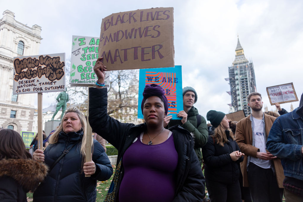 A protester holds a placard that reads 'black lives midwives...
