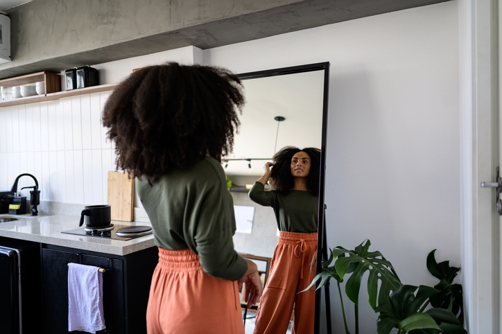 A black woman in the mirror looking at her hair
