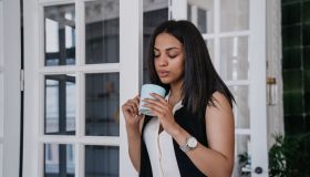 Serious tAfrican american young woman having break holding cup of coffee smiling leaning on door at office. Cheerful Brazilian businesswoman relaxing at home, business and education.