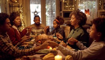African American extended family saying grace while having Thanksgiving meal at dining table.