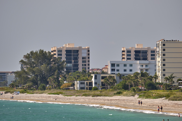 Resort beach with white sand, blue water, tall hotel buildings. Happy people sunbathing and swimming in ocean